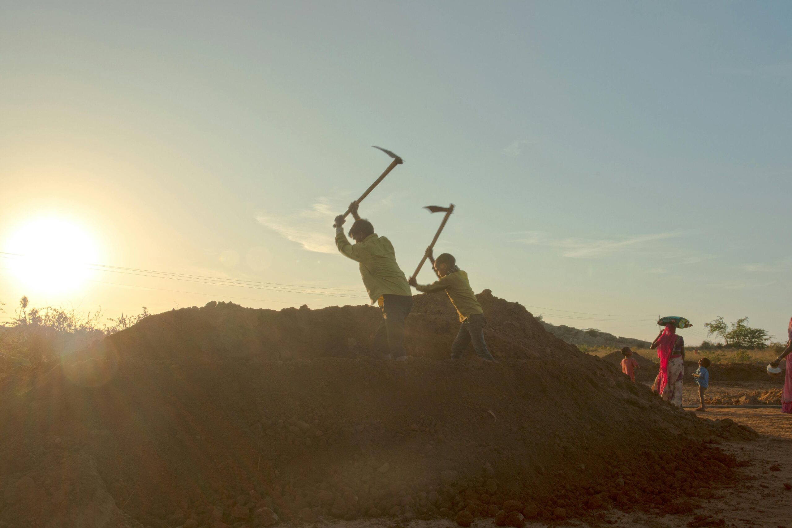 Silhouetted workers laboring at sundown in a rural Indian field, capturing daily life and environment.