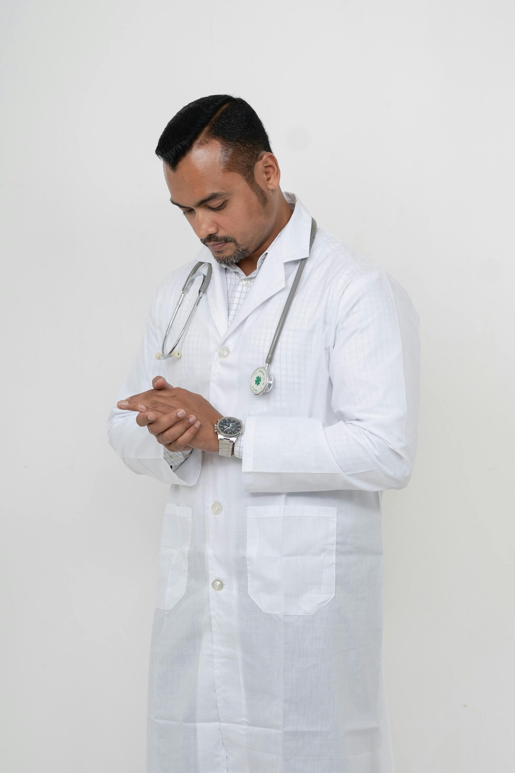 Young male doctor in a white coat, deep in thought with stethoscope in Dhaka hospital.