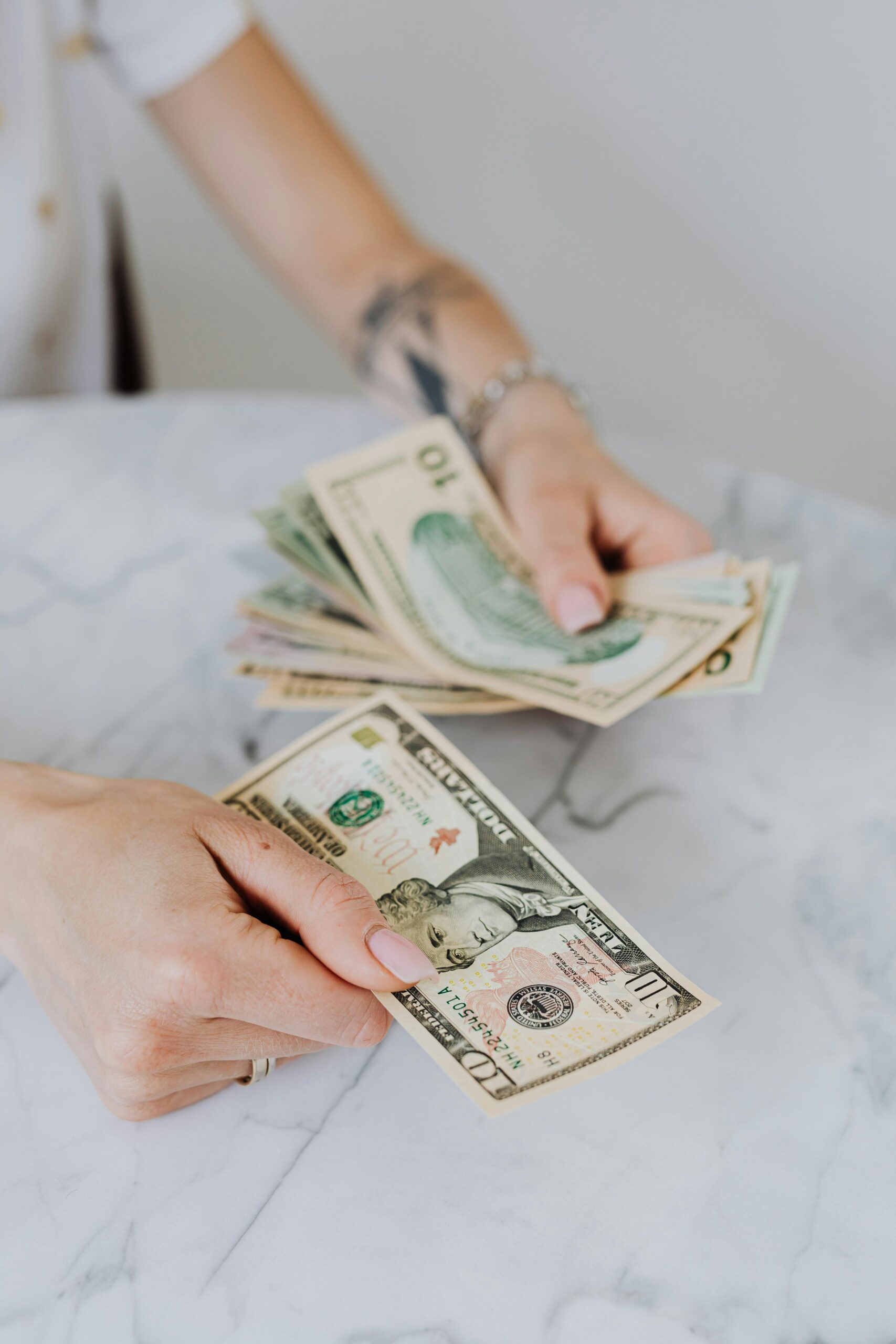Close-up of hands counting US dollar bills on a marble table, symbolizing personal finance.